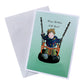 Greeting card and envelope with an illustration of a toddler in a swing looking happy in a dark coat and green trousers. Swing is orange with a black seat and chains. Background is bright green. 