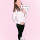 Illustration of a pregnant girl with a little bump, wearing a white top and black trousers, holding a sign saying Mother to be. The background is pink. 